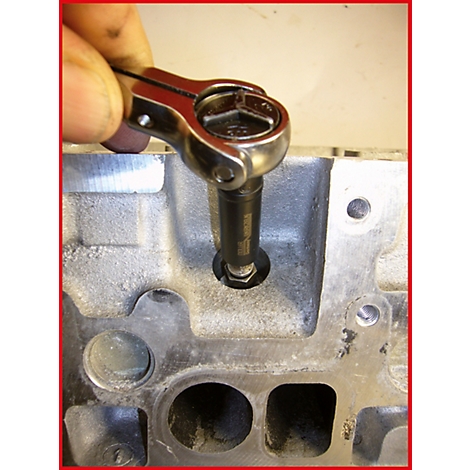 Eine Hand hält eine Ratsche, die eine Schraube in ein Motorenbauteil dreht.